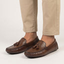 Brown loafers with tassels worn with beige pants on a light background