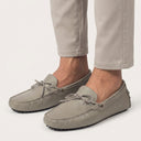 Beige grey loafers worn with beige pants on a light gray background
