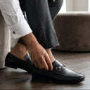 Man adjusting his black shoes in a room with neutral decor