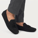 Black loafers with tassels worn with gray pants on a white background