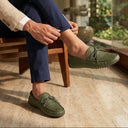 Man sitting on a wooden chair wearing green loafers in a modern indoor setting.
