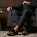 Man in a dark suit sitting on a gray armchair with a glass of water on a table.