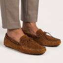Brown suede loafers worn with beige pants on a light background