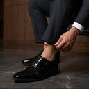 Man in a black suit sitting on a chair, adjusting his black shoes.