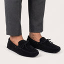 Black suede loafers worn with gray pants on a light background