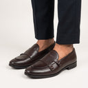 Brown leather loafers worn with dark pants on a light background
