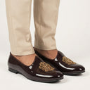 Dark brown loafers with gold detailing worn with beige pants on a white background. wedding jutti shoes