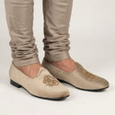 Beige loafers with gold embroidery worn with beige pants on a light gray background. wedding juttis men