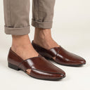 Brown leather shoes worn with rolled-up beige pants on a light background