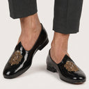 Black glossy loafers with gold embroidery on a white background