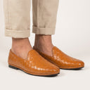 Brown woven loafers worn with beige pants on a white background