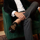 Man in formal attire sitting on a green armchair in an elegant room.
