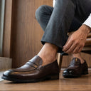 Man sitting in a chair wearing brown loafers, gray pants, and a white shirt.
