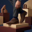 Brown suede shoes worn with gray pants on a geometric background