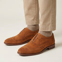 Brown suede brogue shoes worn with beige pants on a light background