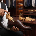 Man in a suit holding a brown leather shoe with wooden insole in a clothing store. cedar wood shoetrees for shoe care.