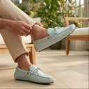 Man sitting on a bench wearing light blue loafers in a bright, indoor setting with plants.
