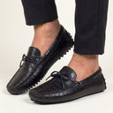 Black leather loafers worn with black pants on a light background