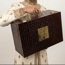 Man holding a wooden briefcase with gold accents on a plain background. shoe gifting luxury box. wedding box. shore care.
