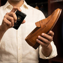 Man holding a brown leather shoe and a black device with a brand logo in a room with shelves. shoe care. shoe sanitizer. feel health. hygiene for shoes.