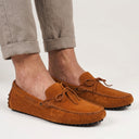 Brown suede loafers worn with beige pants on a light gray background