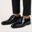 Black patent leather shoes worn with black pants on a light gray background