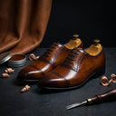 Pair of brown leather shoes on a dark surface with shoe polish and a brush.