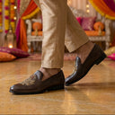 Person wearing brown loafers with decorative elements in a festive indoor setting.
